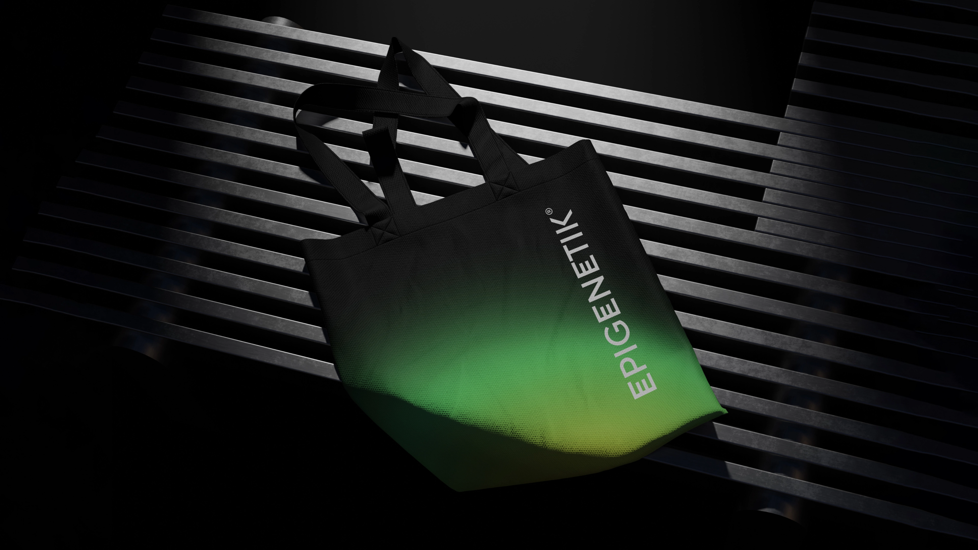 Czarna torba materiałowa z nadrukiem logo Epigenetik i zielonym gradientem, leżąca na metalowej ławce