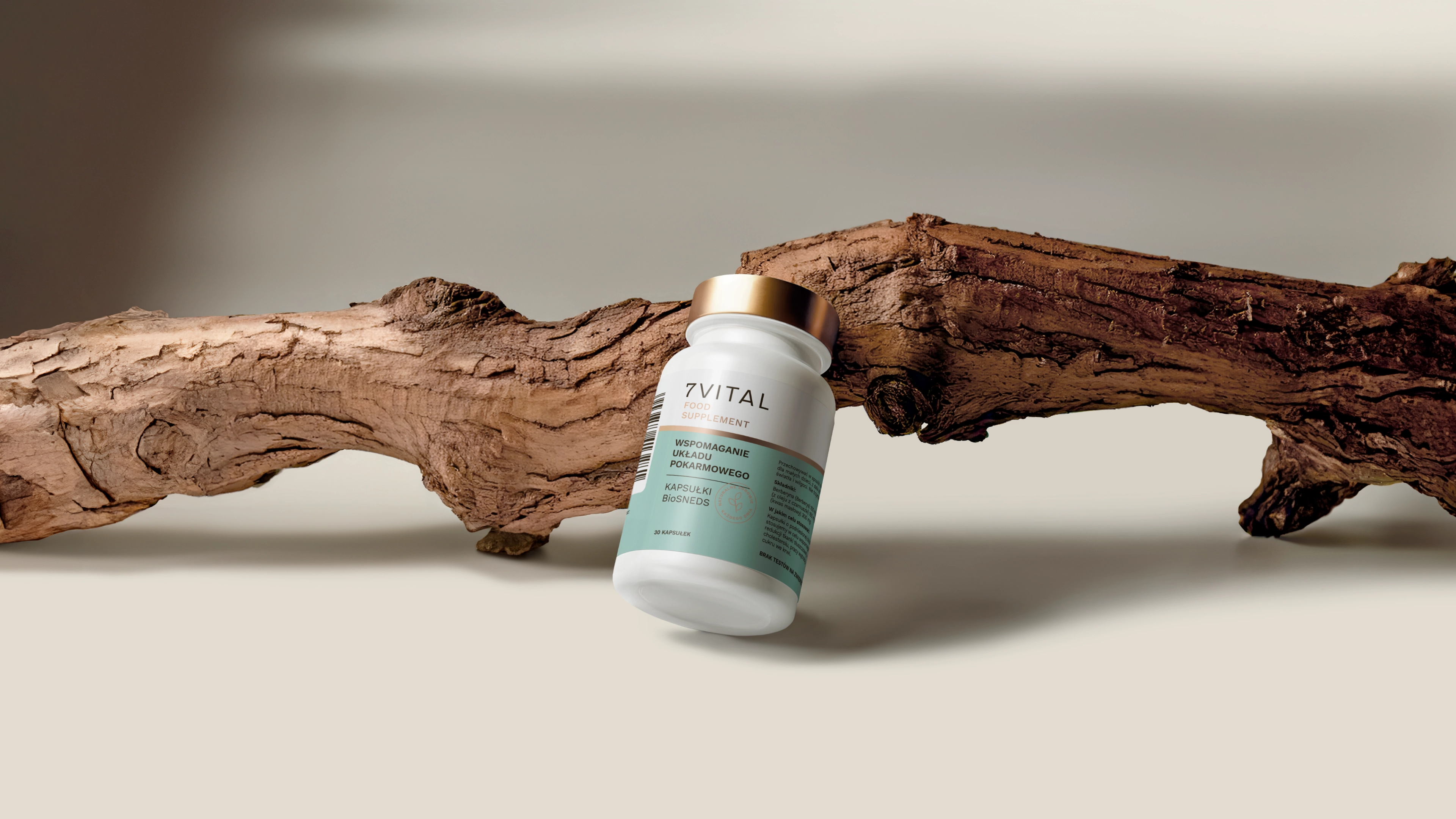 Białe opakowanie suplementu 7Vital z zieloną etykietą ustawiona na tle suchej gałęzi drewna