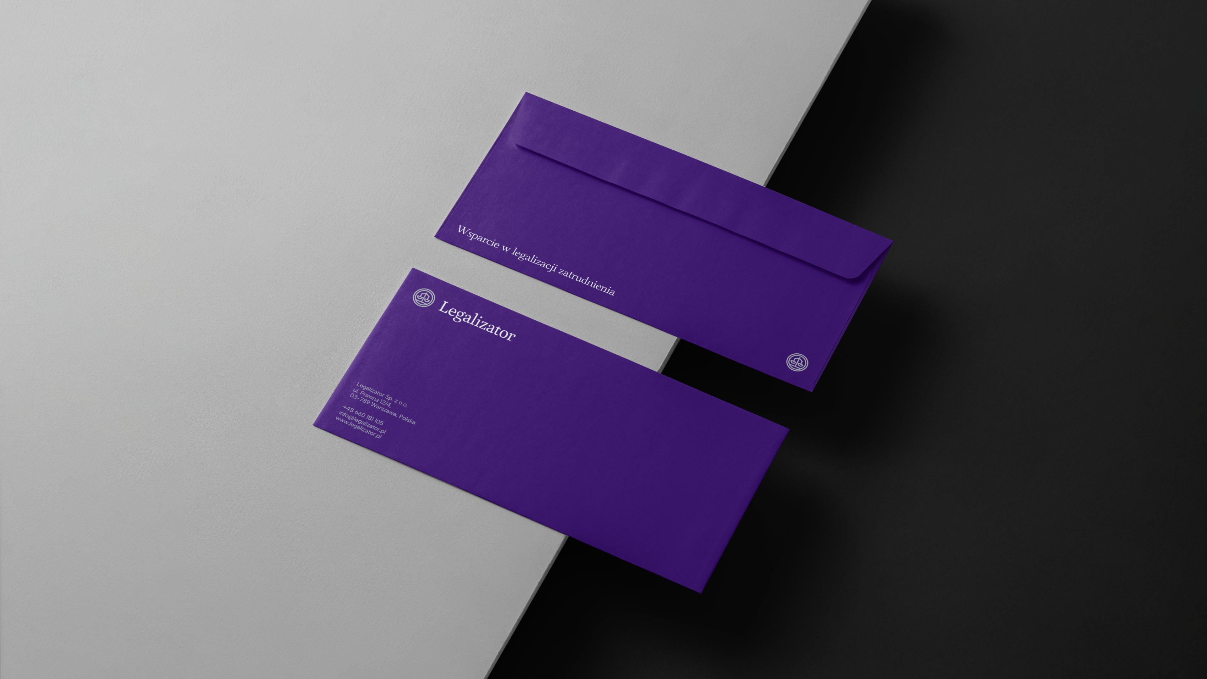 Fioletowe koperty i papeteria Legalizator ułożone na kontrastowym jasnym i ciemnym tle.