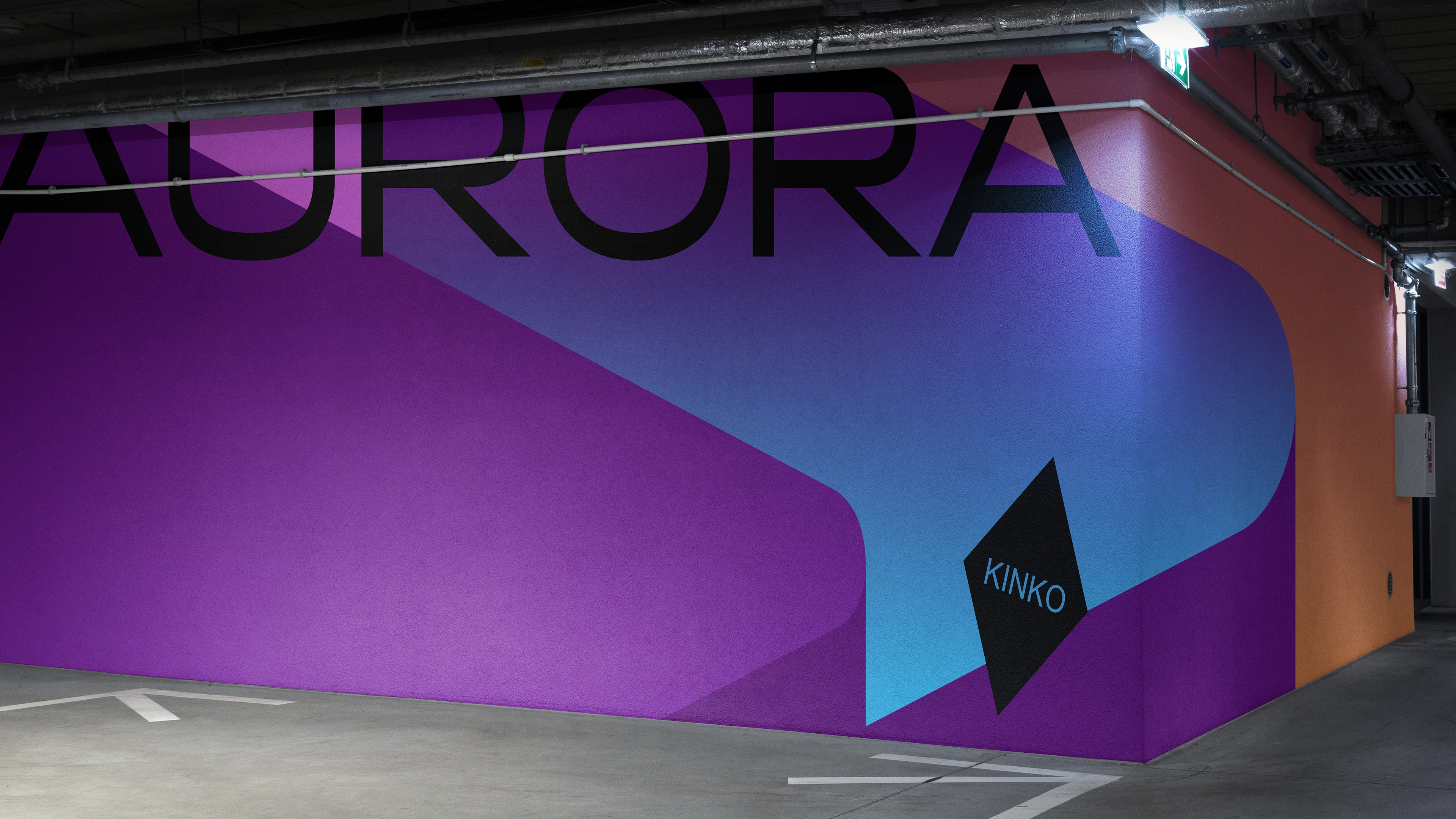 Wielkoformatowa realizacja KINKO Aurora na ścianie garażu podziemnego z dominującą typografią i kolorem.