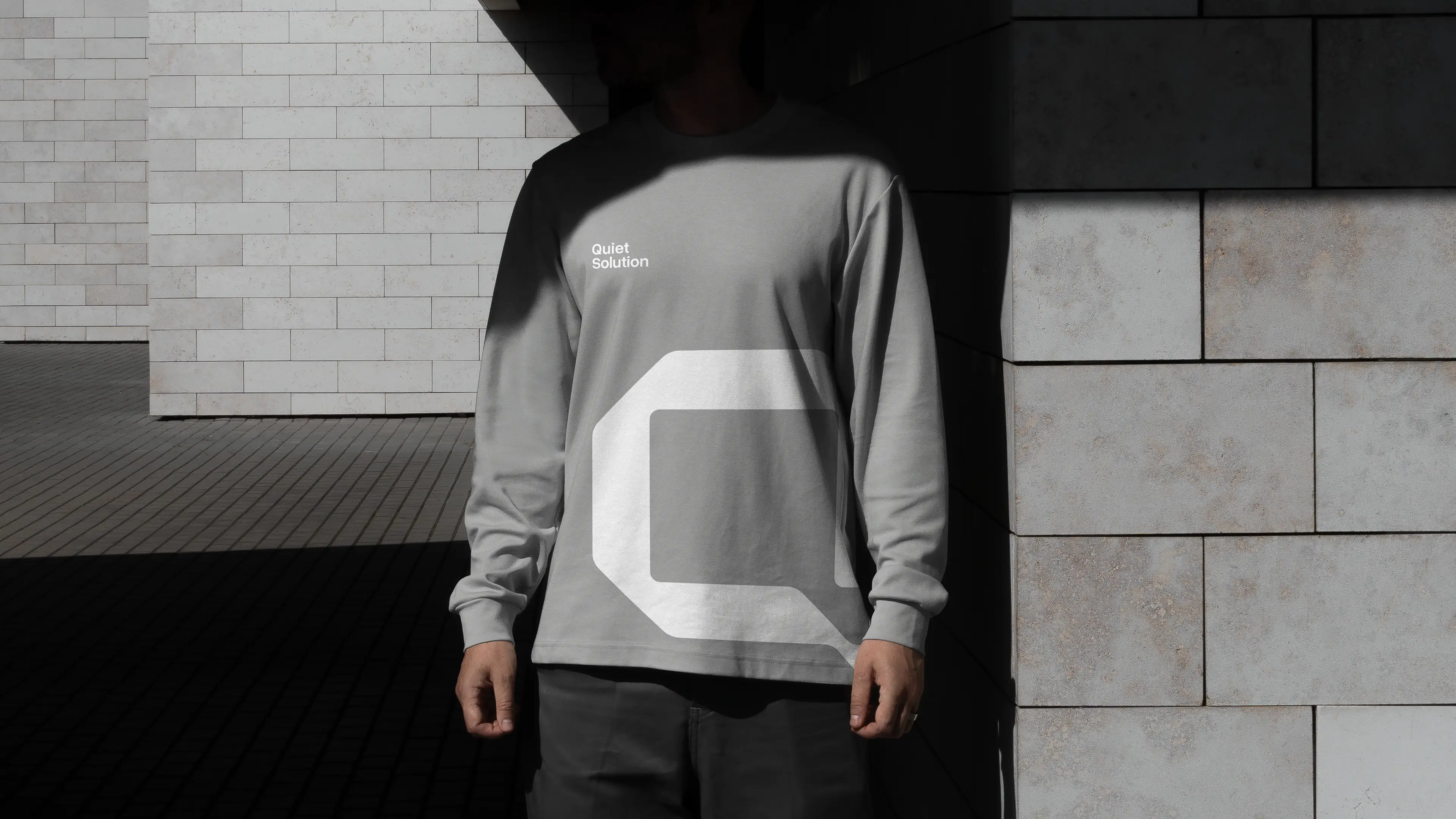 Koszulka Quiet Solution z dużym sygnetem marki na tle architektonicznej przestrzeni.